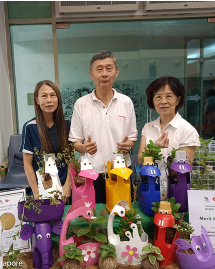 A posed photo of three people standing behind their booth featuring upcycled planters from detergent bottles.